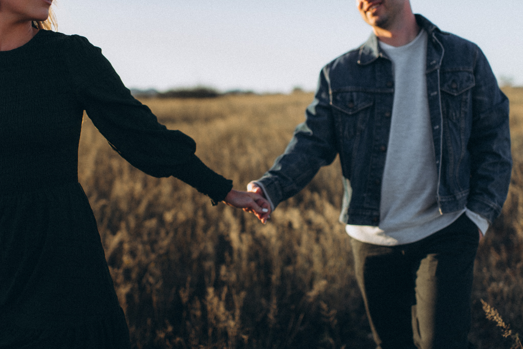 couple walking through arizona field wearing jean jacket and dress