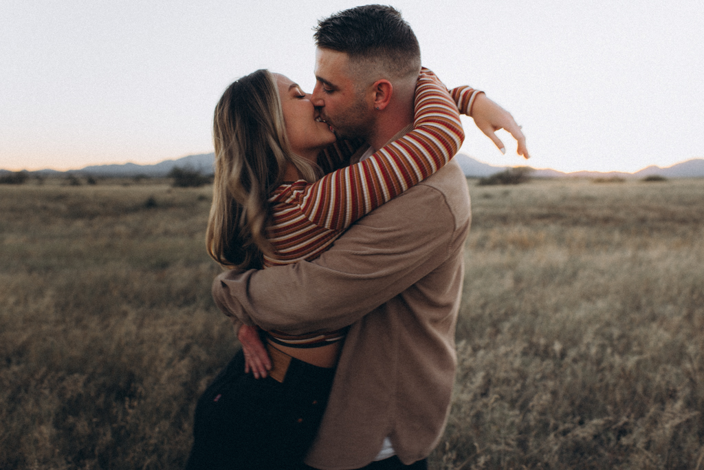 Tips for Family Photo outfits, couple wearing striped shirt and jacket leaning in and kissing in a field in arizona